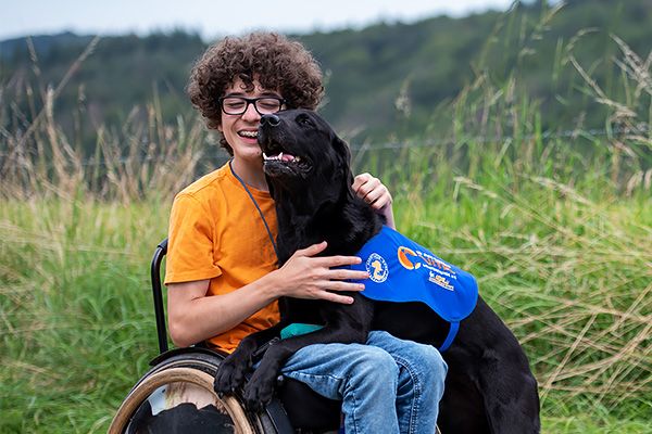 Ein Junge in einem Rollstuhl umarmt glücklich seinen schwarzen Assistenzhund.